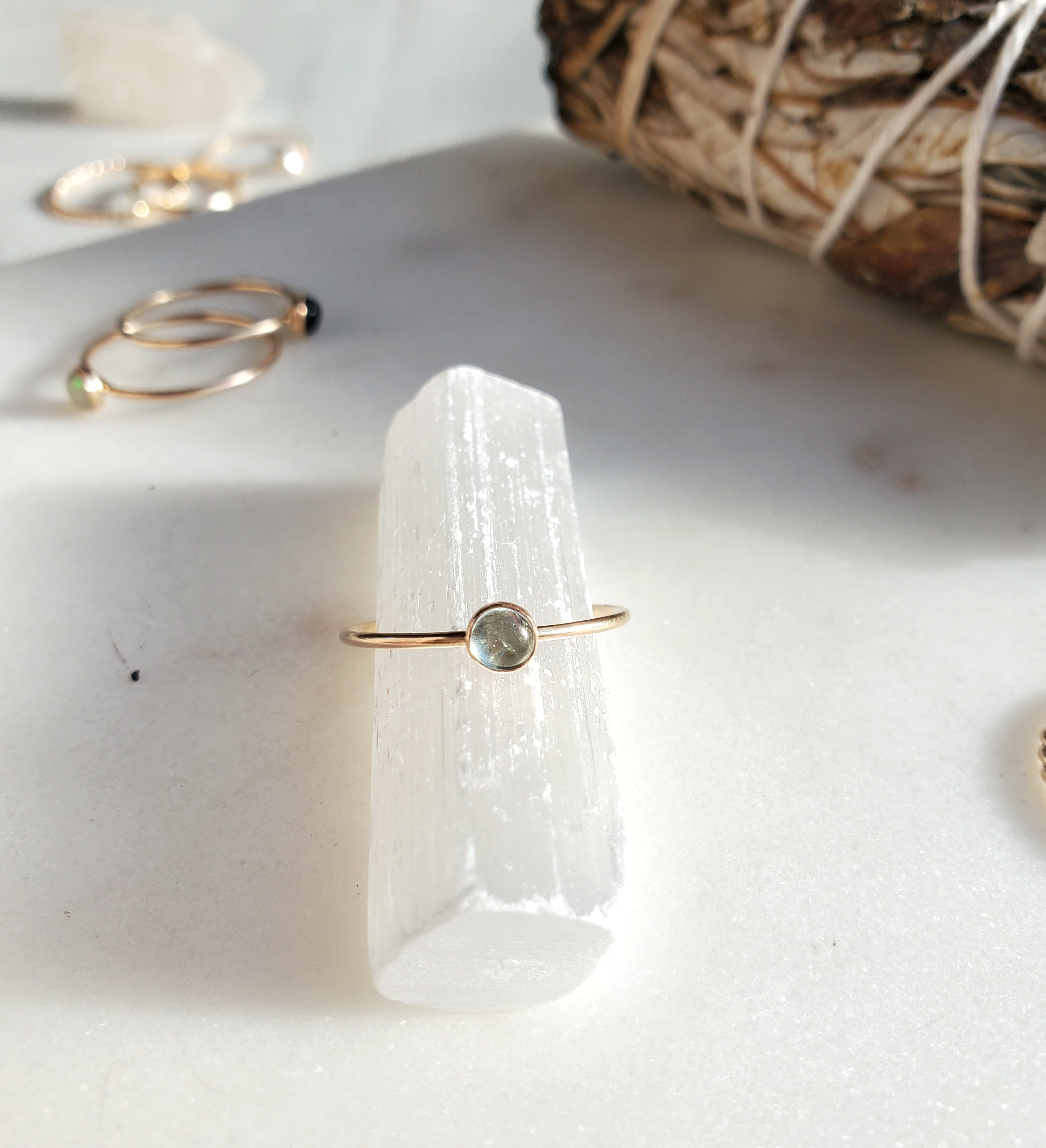 Moonstone and gold ring on a selenite crystal with sage and other rings in the background sparkling in the sun
